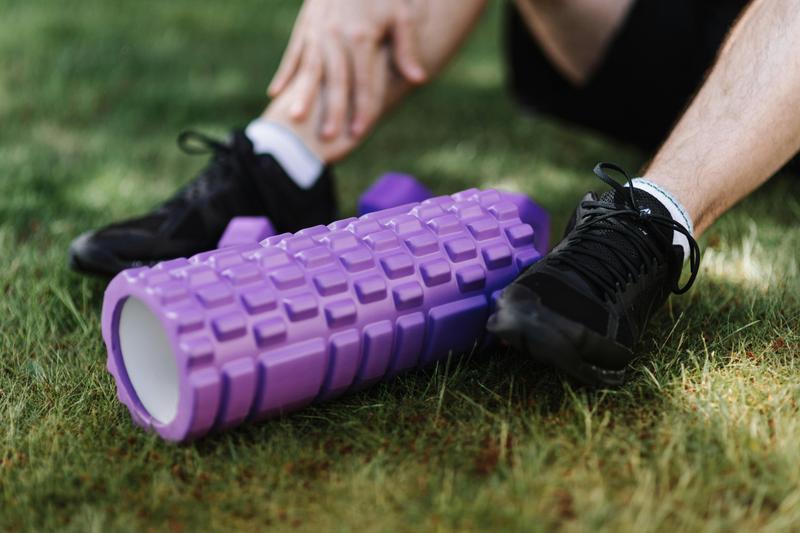 Athlete with black shoes sitting near a purple foam roller